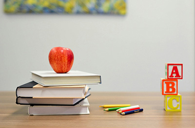 Picture representing children's learning materials books, pencils, apple and building blocks.